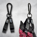 Two black First Earth Flow Star carabiner clips on a concrete background, the right one clipped to a folded red and black Flow Star