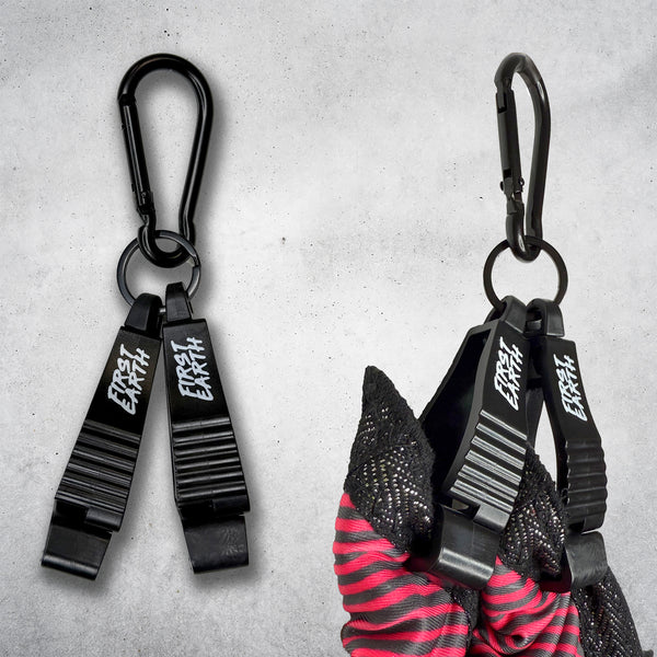 Two black First Earth Flow Star carabiner clips on a concrete background, the right one clipped to a folded red and black Flow Star