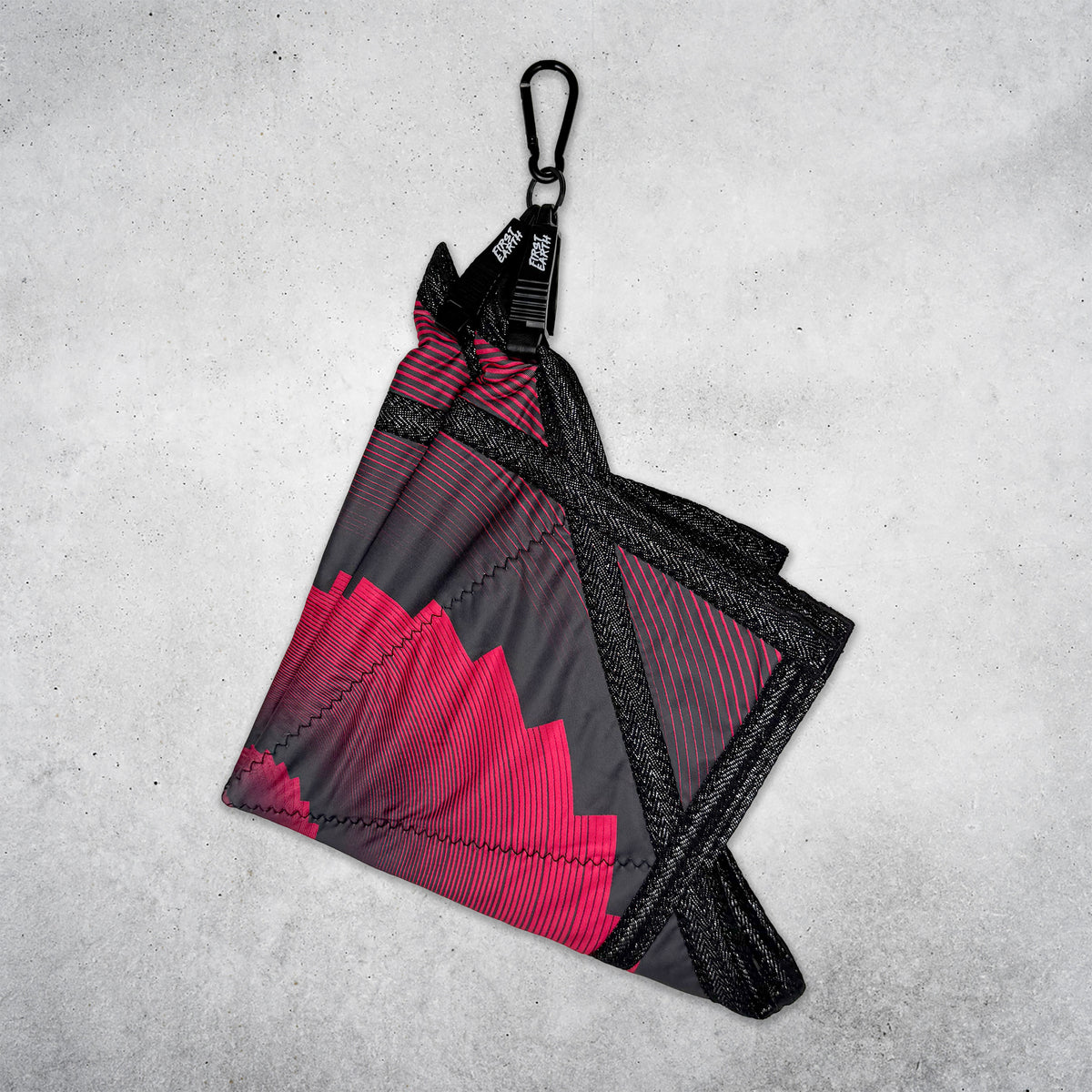 Folded red and black Flow Star hanging from a black First Earth Flow Star carabiner against a concrete wall