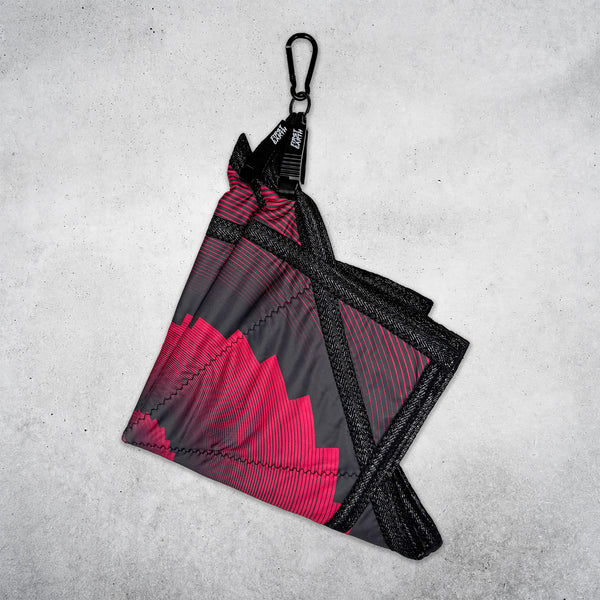 Folded red and black Flow Star hanging from a black First Earth Flow Star carabiner against a concrete wall