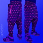 First Earth Asanoha Pink velvet harem joggers under UV blacklight on model showing glowing pink geometric asanoha pattern