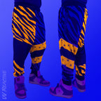 First Earth Sacred Stripes velvet harem joggers under UV blacklight on model showing glowing orange tiger stripes and geometric panels