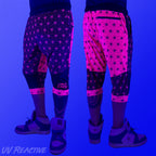 First Earth Asanoha Pink 3/4 velvet harem shorts under UV blacklight on model, showing front and back glowing pink pattern