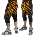 First Earth Sacred Stripes three-quarter velvet harem shorts on model, showing front and back views with orange tiger stripes and geometric panels