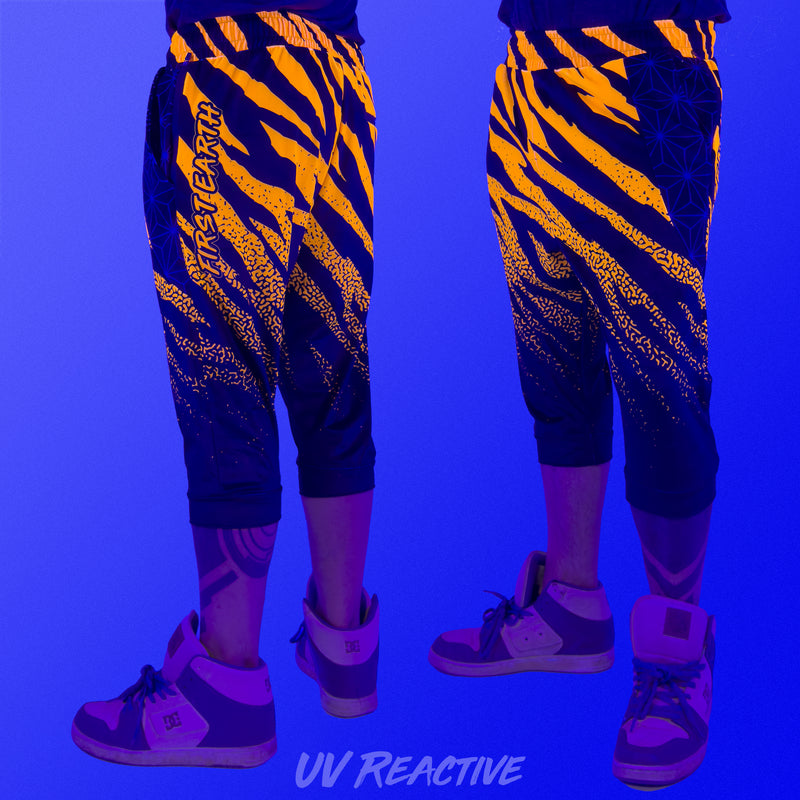First Earth Sacred Stripes 3/4 velvet harem shorts under UV blacklight on model, showing front and back with glowing orange tiger stripes