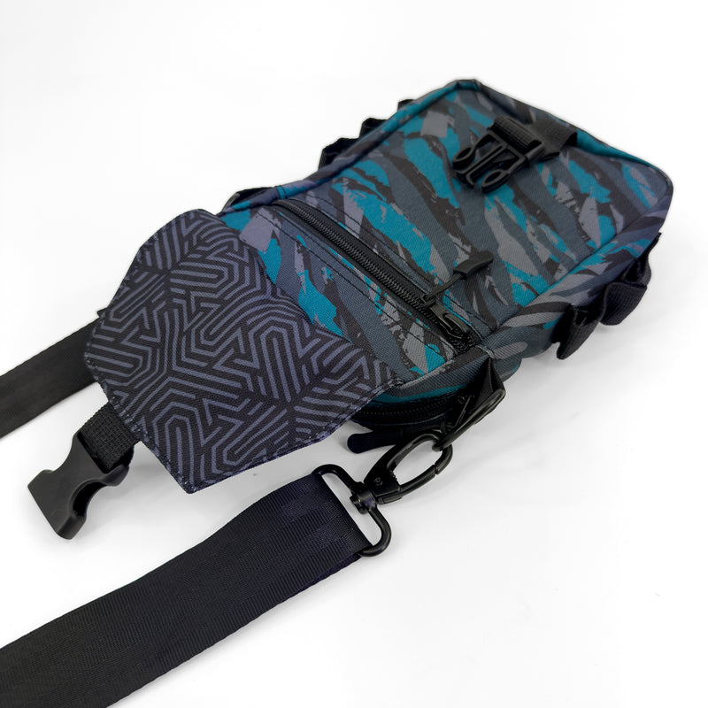 First Earth Shadow sling bag front view with flap open, zipper pocket, buckle, and strap hardware