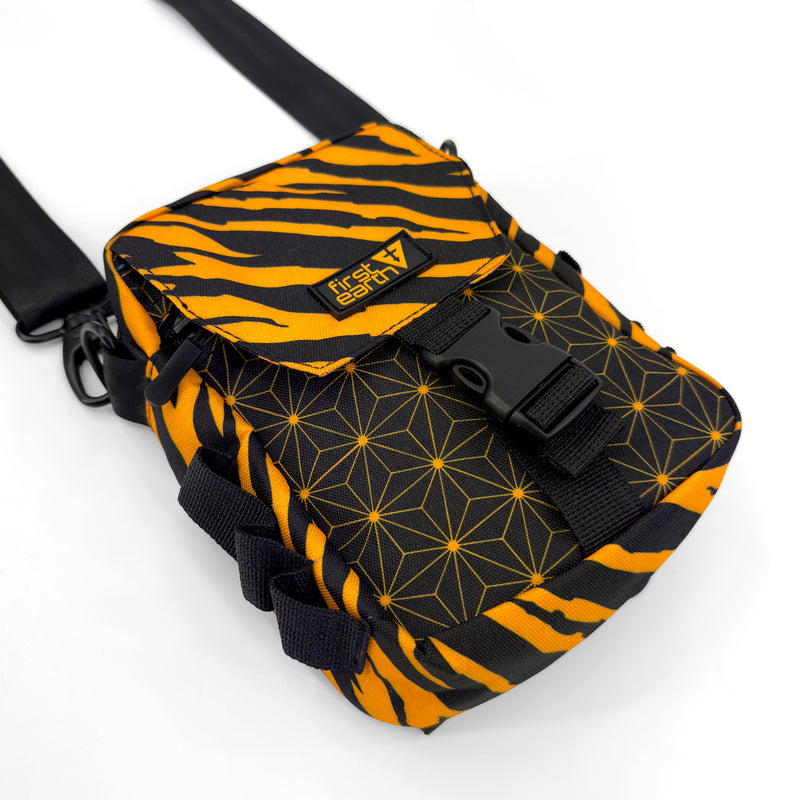 First Earth Sacred Stripes UV sling bag front with orange tiger stripes, black buckle, and geometric pattern
